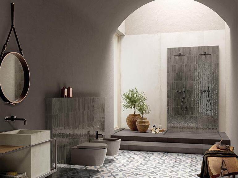 Nell’immagine, raffinato ambiente bagno realizzato con GLIM, una collezione vitaminica capace di decorare gli ambienti con il colore, grazie a brick smaltati dal finish brillante. La parete doccia e quella antistante i sanitari sono rivestite con la finitura Grigio Fumo (6x24cm), tonalità che con le sue molteplici sfumature infonde un senso di profondo equilibrio. I brick glossy di GLIM si accostano con eleganza al delicato effetto cemento Ylico, Light, nel maxi-formato 120x278. A pavimento, il fascino retr